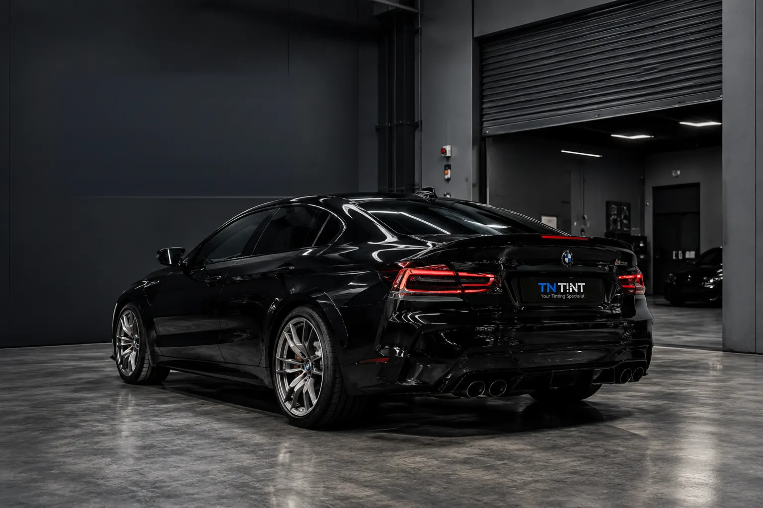 A black sedan with tinted windows in the TN TINT workshop in Clayton South, seen from the rear three-quarter angle.